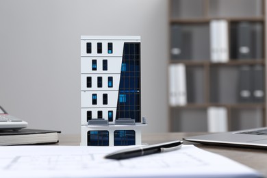 Photo of Real estate. Apartment building model, floor plan and laptop on table indoors, selective focus