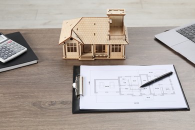 Photo of Real estate. House model, floor plan, laptop and calculator on wooden table, closeup