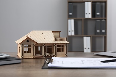 Photo of Real estate. House model and floor plan on wooden table indoors