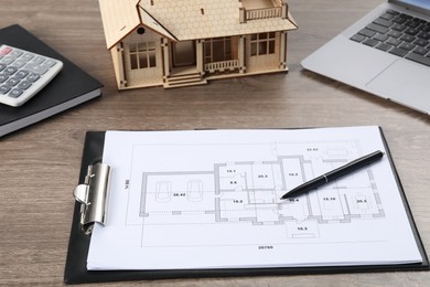Photo of Real estate. House model, floor plan and laptop on wooden table, closeup