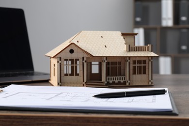 Photo of Real estate. House model, floor plan and laptop on wooden table indoors, closeup