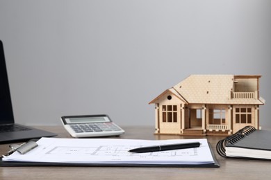 Photo of Real estate. House model, floor plan, laptop and calculator on wooden table. Space for text