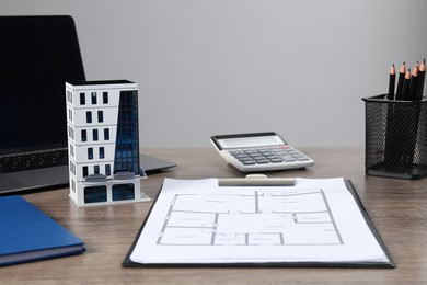 Photo of Real estate. Apartment building model, floor plan and laptop on wooden table