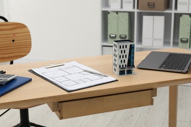 Photo of Real estate. Apartment building model, floor plan and laptop on wooden table indoors