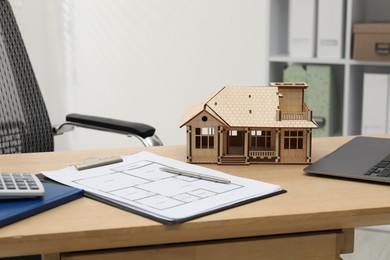 Photo of Real estate. House model, floor plan and laptop on wooden table indoors