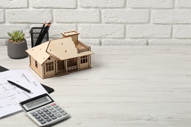 Photo of Real estate. House model, floor plan and calculator on white wooden table. Space for text