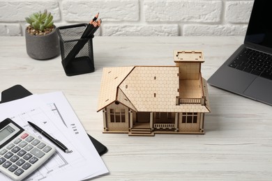 Photo of Real estate. House model, floor plan, calculator and laptop on white wooden table, closeup