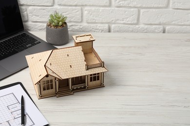 Photo of Real estate. House model, floor plan and laptop on white wooden table, closeup. Space for text