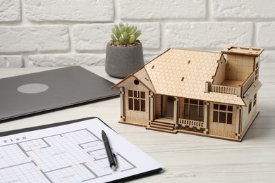 Photo of Real estate. House model, floor plan and laptop on white wooden table, closeup