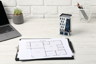Photo of Real estate. Apartment building model, floor plan and laptop on white wooden table, closeup