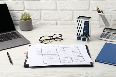 Photo of Real estate. Apartment building model, floor plan, calculator and laptop on white wooden table, closeup