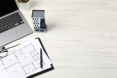 Photo of Real estate. Apartment building model, floor plan and laptop on white wooden table. Space for text