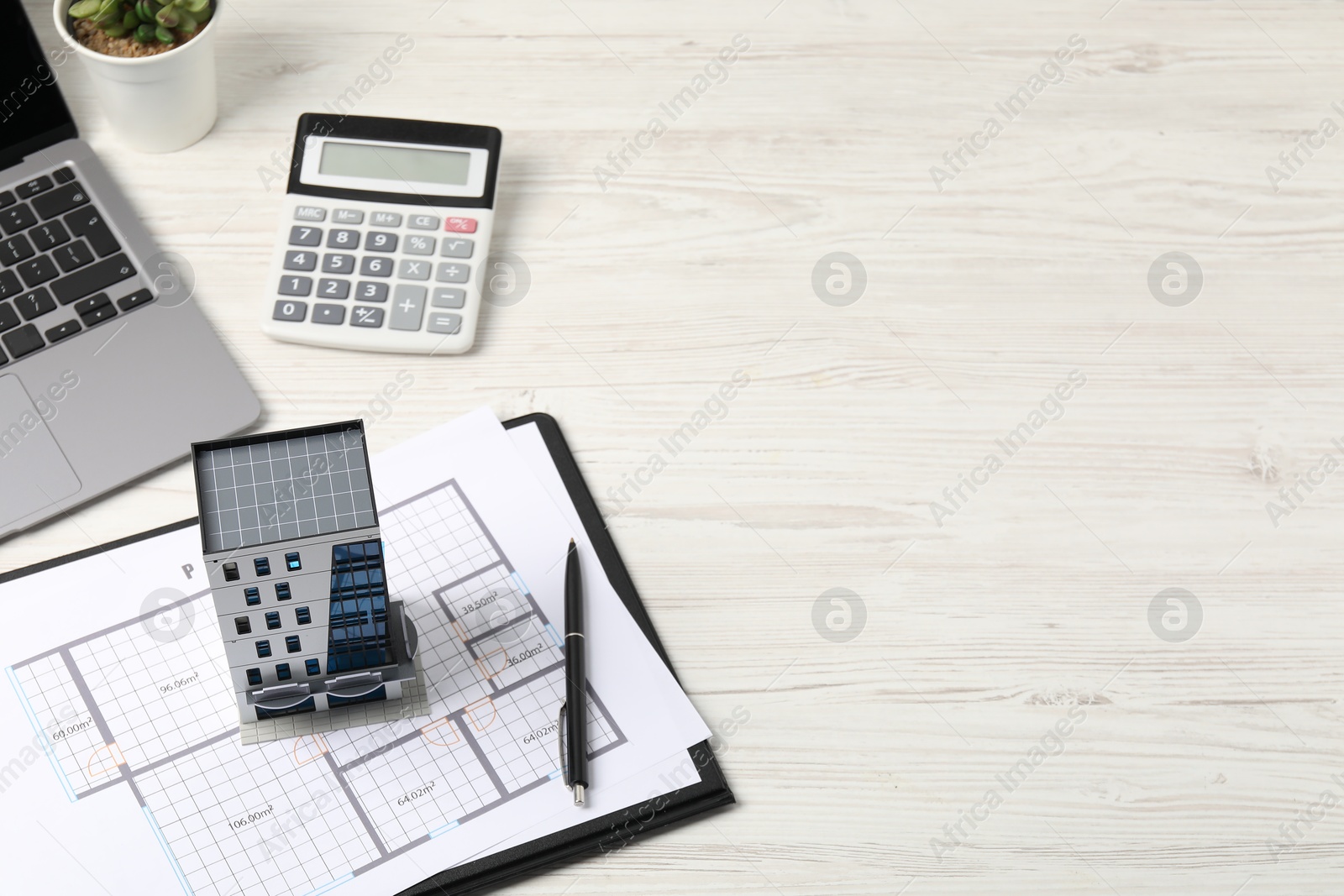 Photo of Real estate. Apartment building model, floor plan, calculator and laptop on white wooden table. Space for text