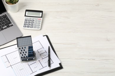 Photo of Real estate. Apartment building model, floor plan, calculator and laptop on white wooden table. Space for text