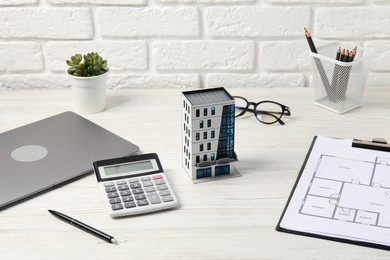 Photo of Real estate. Apartment building model, floor plan, calculator and laptop on white wooden table