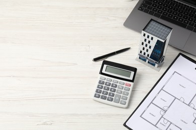 Photo of Real estate. Apartment building model, floor plan, calculator and laptop on white wooden table. Space for text