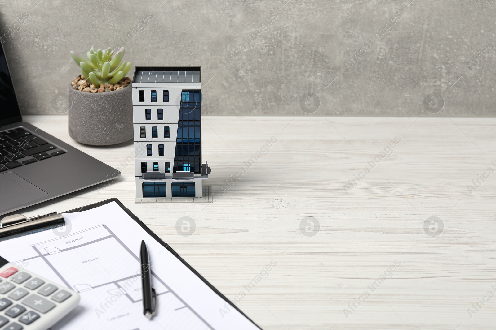 Photo of Real estate. Apartment building model, floor plan, calculator and laptop on white wooden table. Space for text