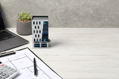 Photo of Real estate. Apartment building model, floor plan, calculator and laptop on white wooden table. Space for text