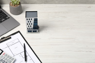 Photo of Real estate. Apartment building model, floor plan, calculator and laptop on white wooden table. Space for text