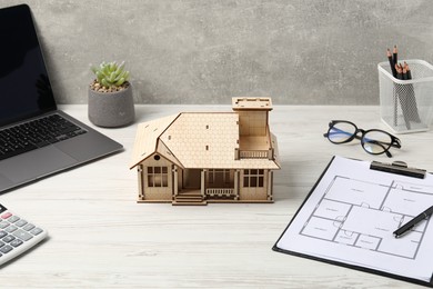 Photo of Real estate. House model, floor plan and laptop on white wooden table