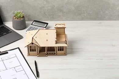 Photo of Real estate. House model, floor plan, calculator and laptop on white wooden table, space for text