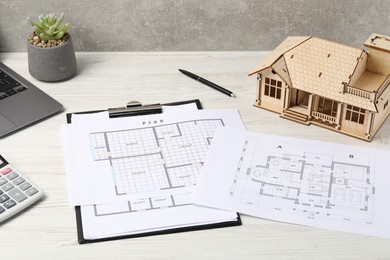 Photo of Real estate. House model, floor plan and laptop on white wooden table