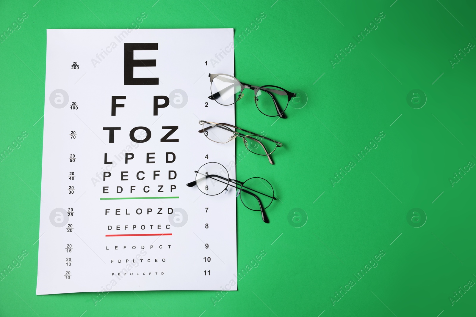Photo of Vision test chart and glasses on green background, flat lay. Space for text