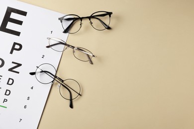 Photo of Vision test chart and glasses on beige background, flat lay. Space for text