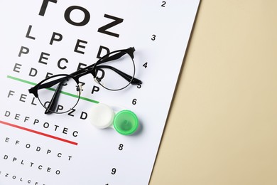 Photo of Vision test chart, glasses and lenses on beige background, top view. Space for text