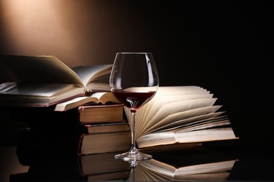Photo of Red wine in glass and stack of books on mirror table against dark background, closeup