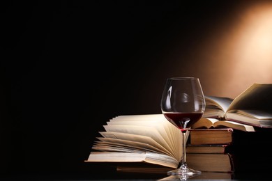 Photo of Red wine in glass and stack of books on mirror table against dark background, closeup. Space for text