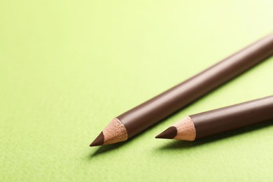 Photo of Brown eyebrow pencils on green background, closeup. Space for text