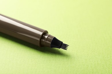 Photo of One liquid eyebrow pencil on green background, closeup. Space for text