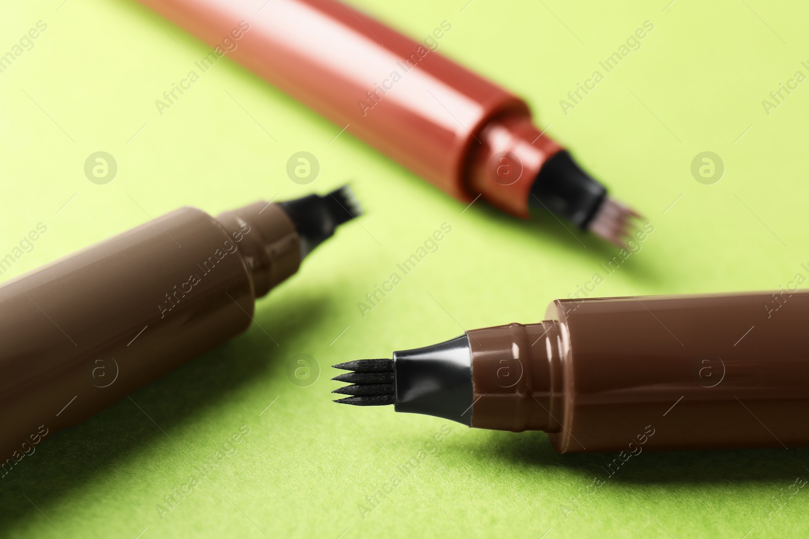 Liquid eyebrow pencils on green background, closeup Photo of Liquid eyebrow pencils on green background, closeup
