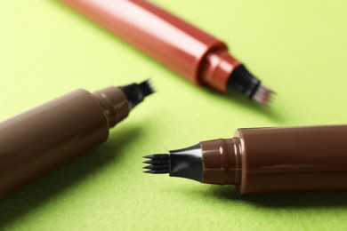 Photo of Liquid eyebrow pencils on green background, closeup