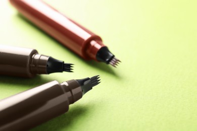 Photo of Liquid eyebrow pencils on green background, closeup. Space for text