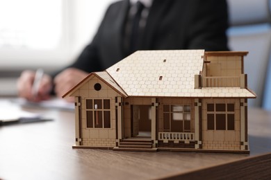 Photo of Real estate agent working at desk in office, focus on house model