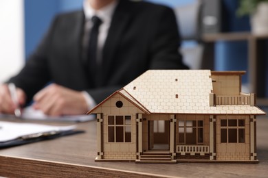 Photo of Real estate agent working at desk in office, focus on house model
