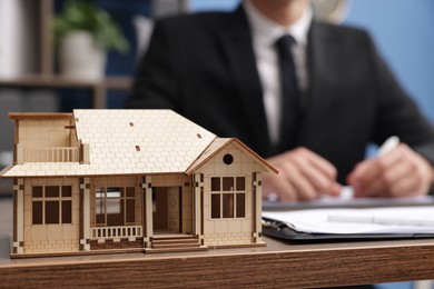 Photo of Real estate agent working at desk in office, focus on house model