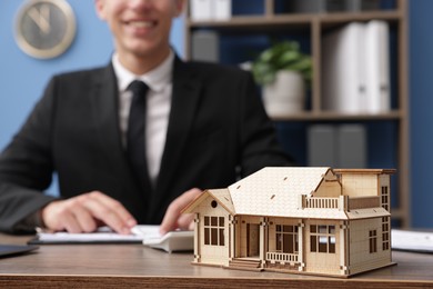 Photo of Real estate agent working at desk in office, focus on house model