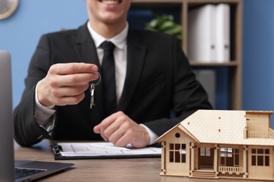 Photo of Real estate agent with house model and key at desk in office, closeup