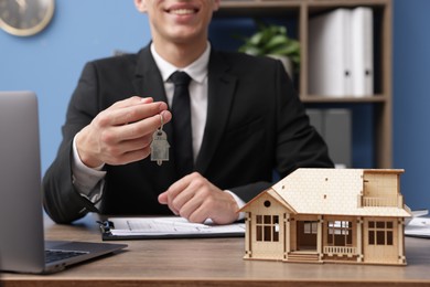 Photo of Real estate agent with house model and key at desk in office, closeup