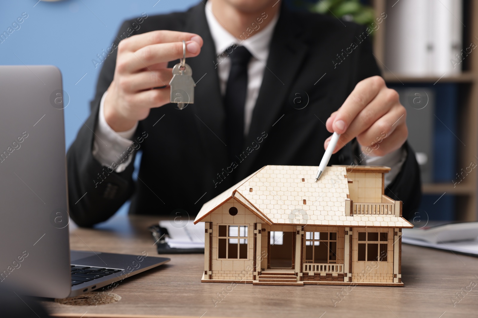 Real estate agent with house model and key at desk in office, closeup Photo of Real estate agent with house model and key at desk in office, closeup