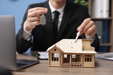 Photo of Real estate agent with house model and key at desk in office, closeup