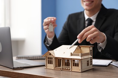 Photo of Real estate agent with house model and key at desk in office, closeup