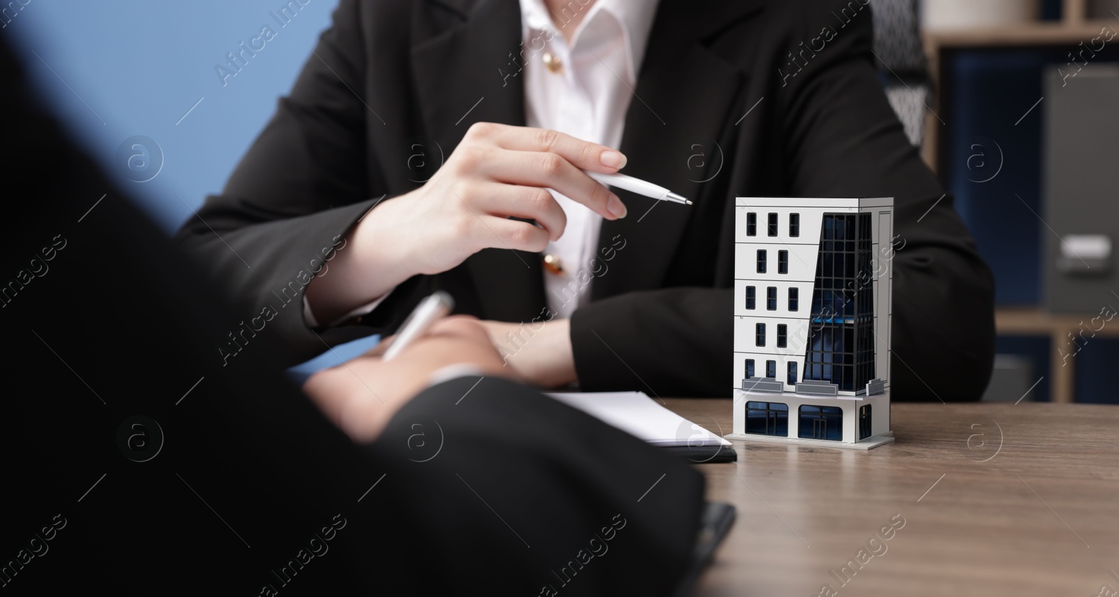 Photo of Real estate agent working with client at desk with house model in office, closeup