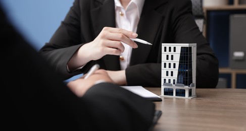Photo of Real estate agent working with client at desk with house model in office, closeup