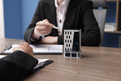Photo of Real estate agent and client at desk in office, focus on house model