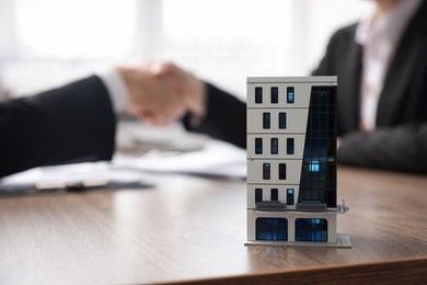 Photo of Real estate agent and client shaking hands at desk in office, focus on house model