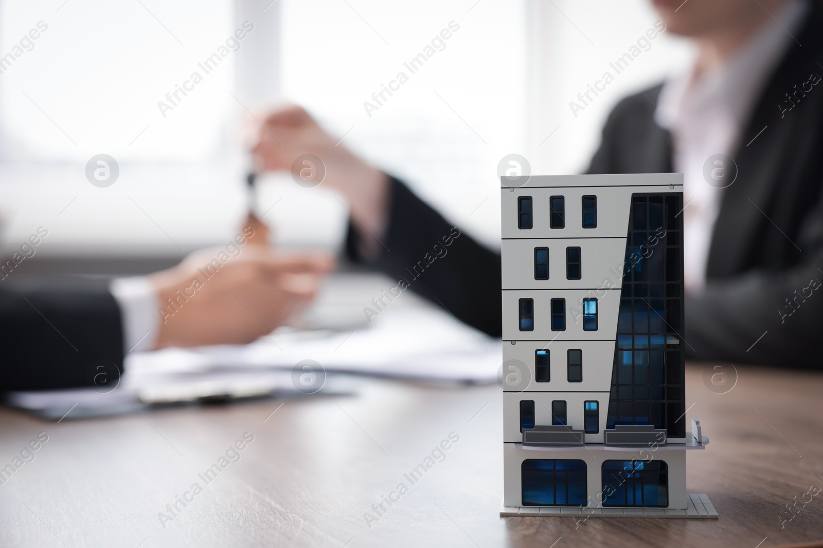 Real estate agent giving key to client at desk in office, focus on house model Photo of Real estate agent giving key to client at desk in office, focus on house model